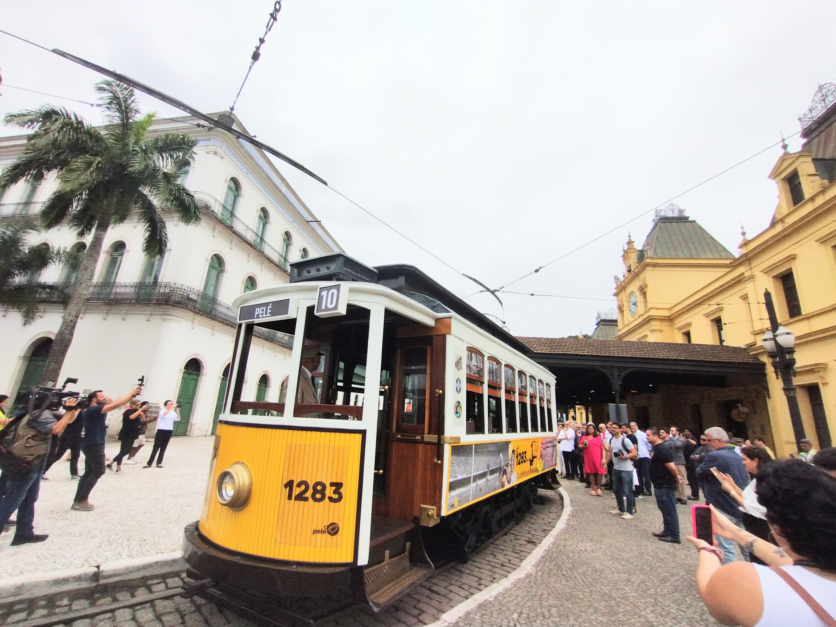 Bonde Pelé, amarelo e branco, fechado, em frente à estação no centro histórico de Santos.