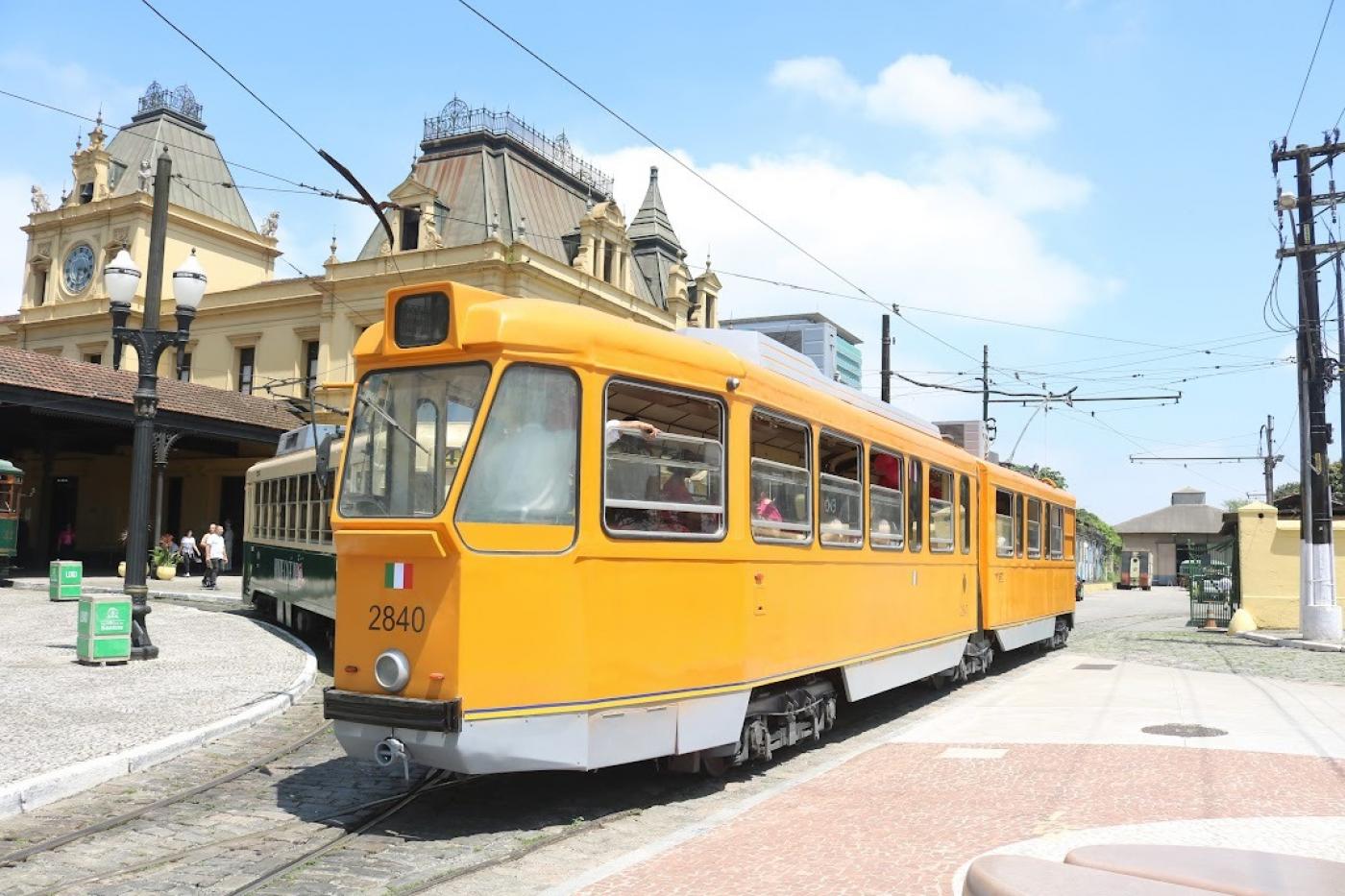 Bonde turístico alaranjado, fechado, próximo à estação no centro histórico de Santos.