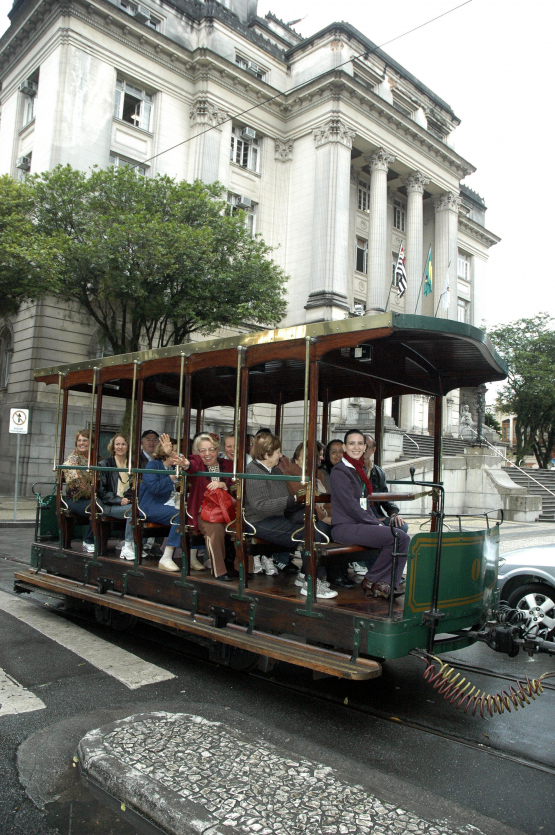 Reboque de bonde, na cor verde, repleto de passageiros, com o Paço Municipal ao fundo, na Praça Mauá, no centro de Santos