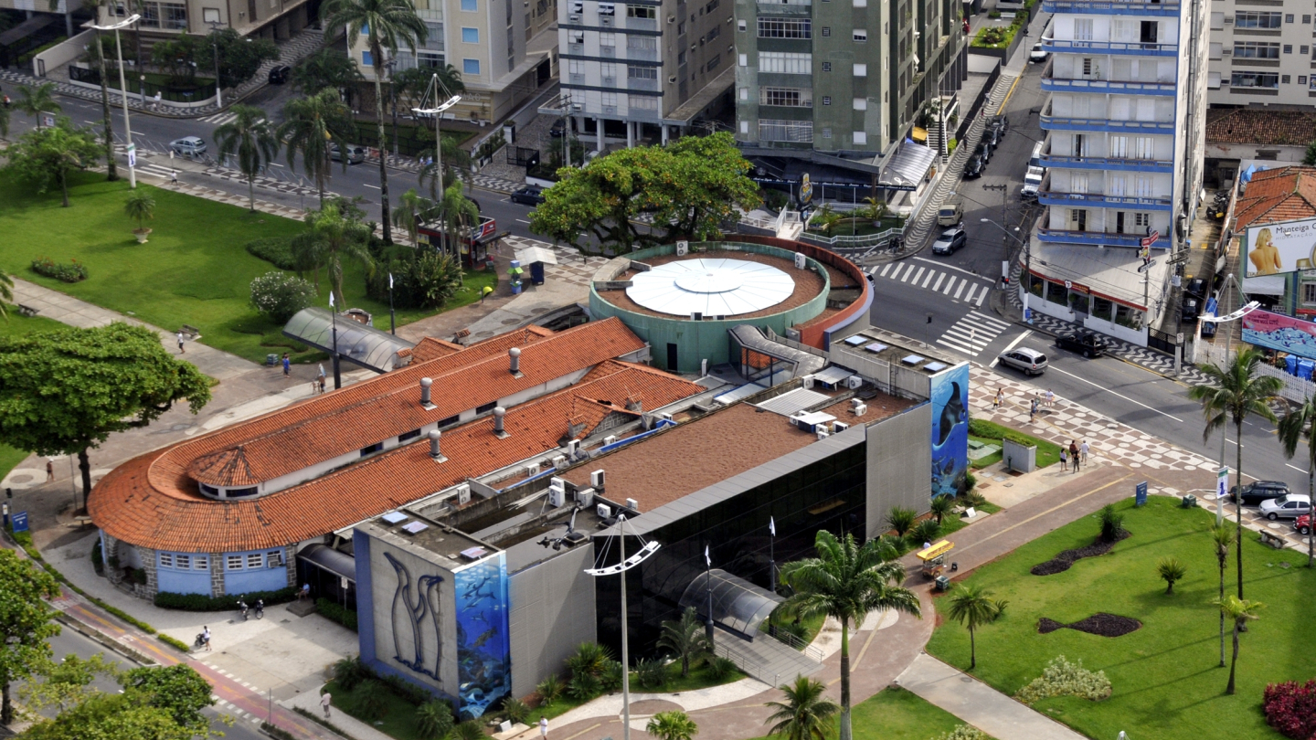 Vista aérea do Aquário Municipal de Santos cercado por prédios, áreas verdes e vias urbanas