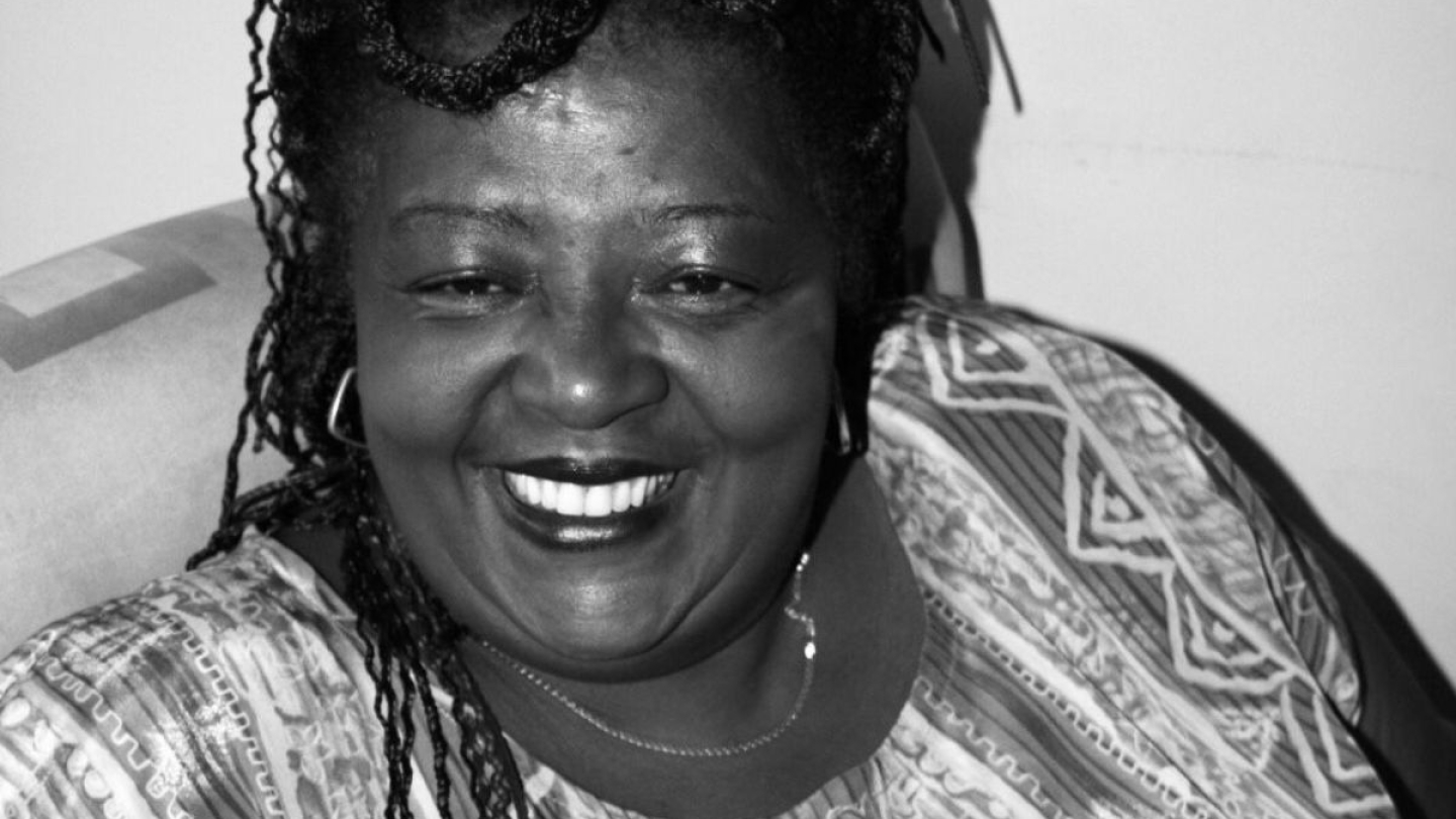 Retrato em preto e branco de uma mulher negra sorridente, com cabelos trançados e usando uma blusa com padrões geométricos.