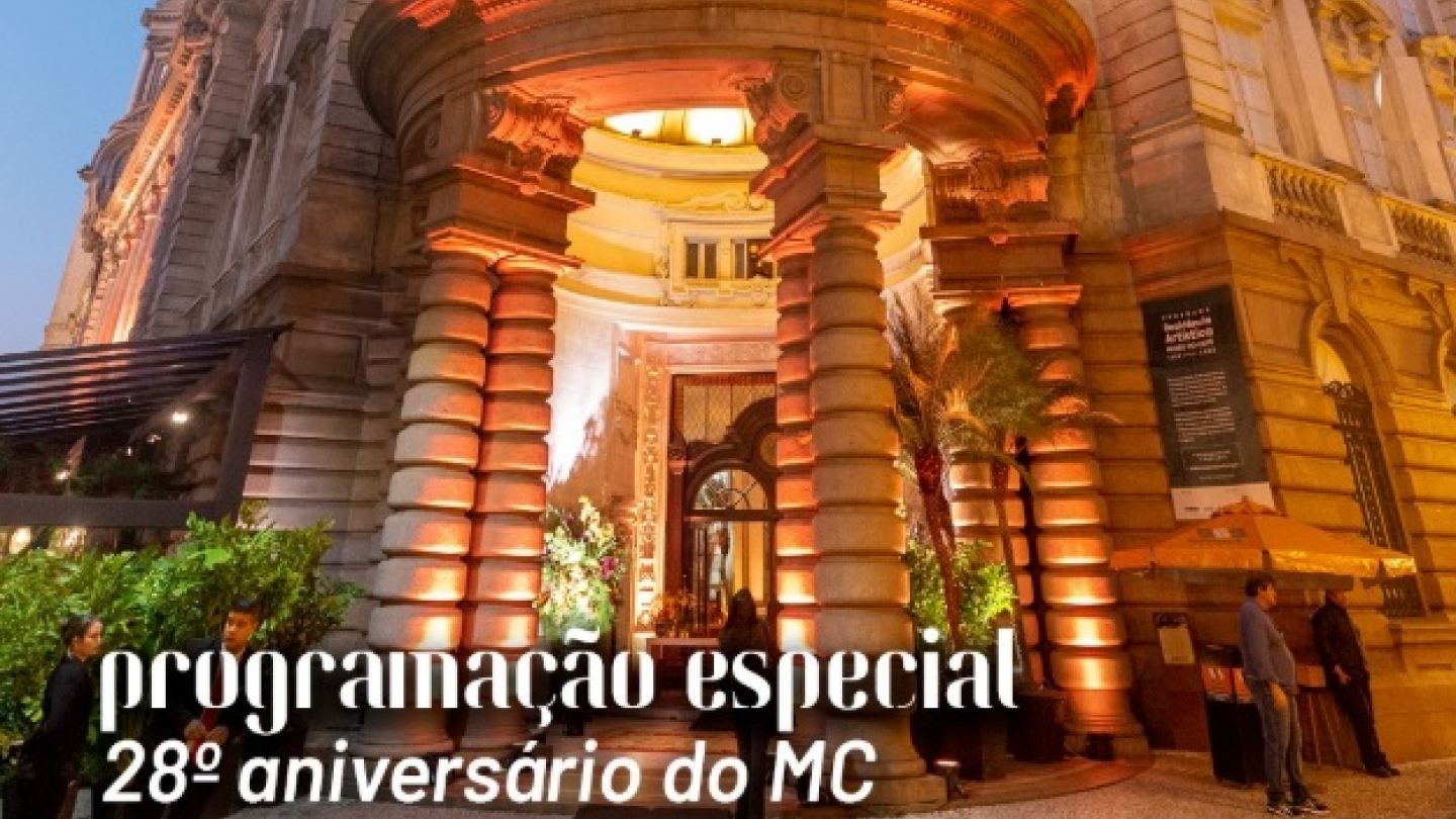 A imagem mostra a fachada histórica iluminada do edifício da antiga Bolsa Oficial de Café, em Santos, anunciando a programação especial do 28º aniversário do Museu do Café