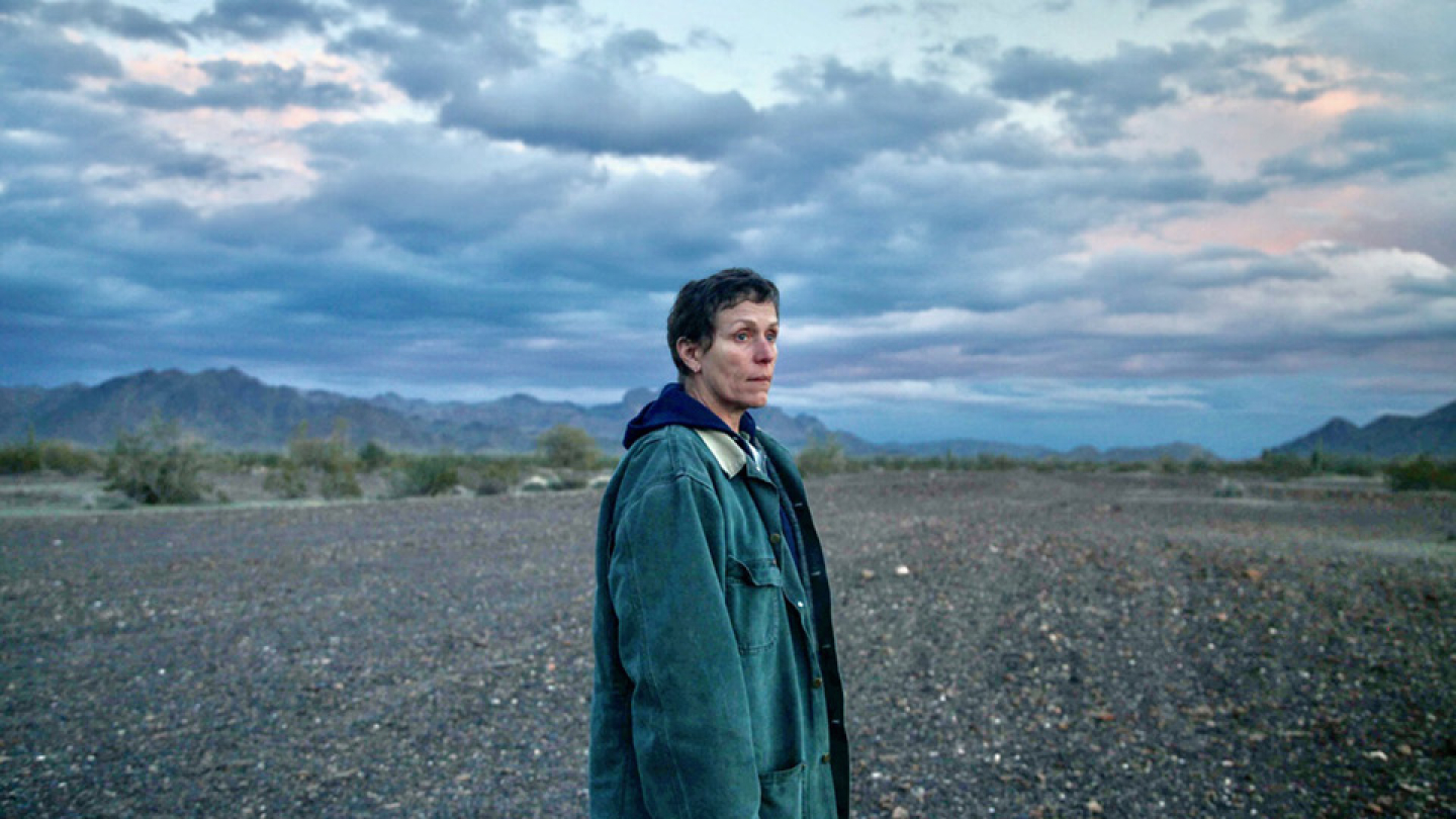 Frances McDormand observa o horizonte em uma vasta e melancólica paisagem desértica sob um céu nublado, em uma cena do filme Nomadland