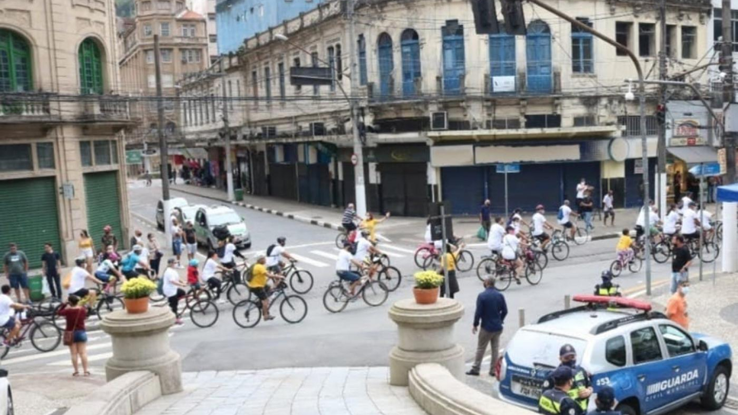 Diversos ciclistas atravessam um cruzamento no Centro Histórico de Santos sob a supervisão da Guarda Civil Municipal durante um passeio ciclístico