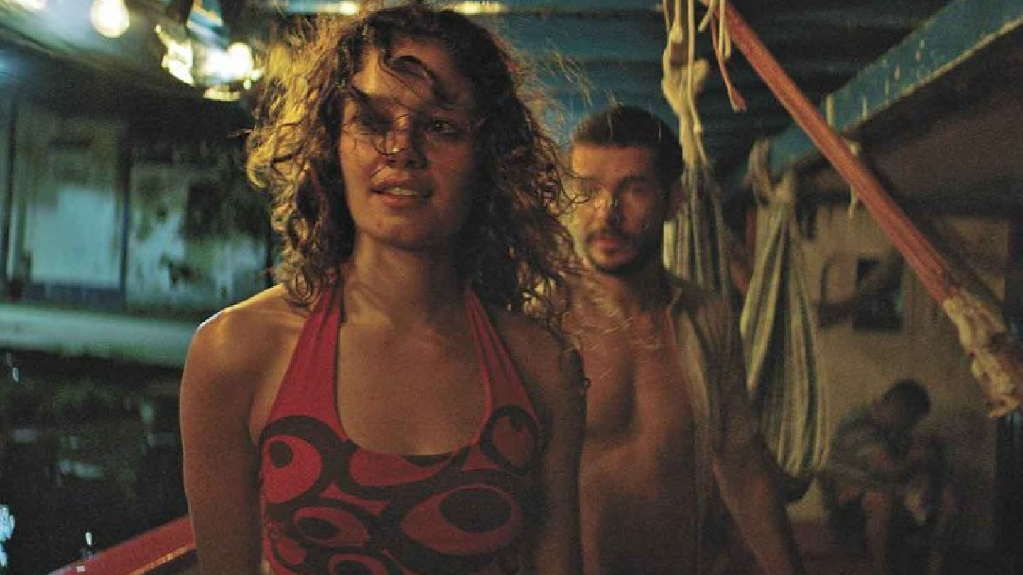Sophie Charlotte e Daniel de Oliveira em uma cena noturna do filme "O Rio do Desejo", a bordo de uma embarcação iluminada por lâmpadas suspensas
