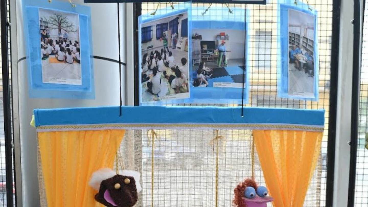 Um painel de "Contação de Histórias" apresenta fotos de atividades educativas e um pequeno teatro de fantoches feitos de meia com cortinas amarelas
