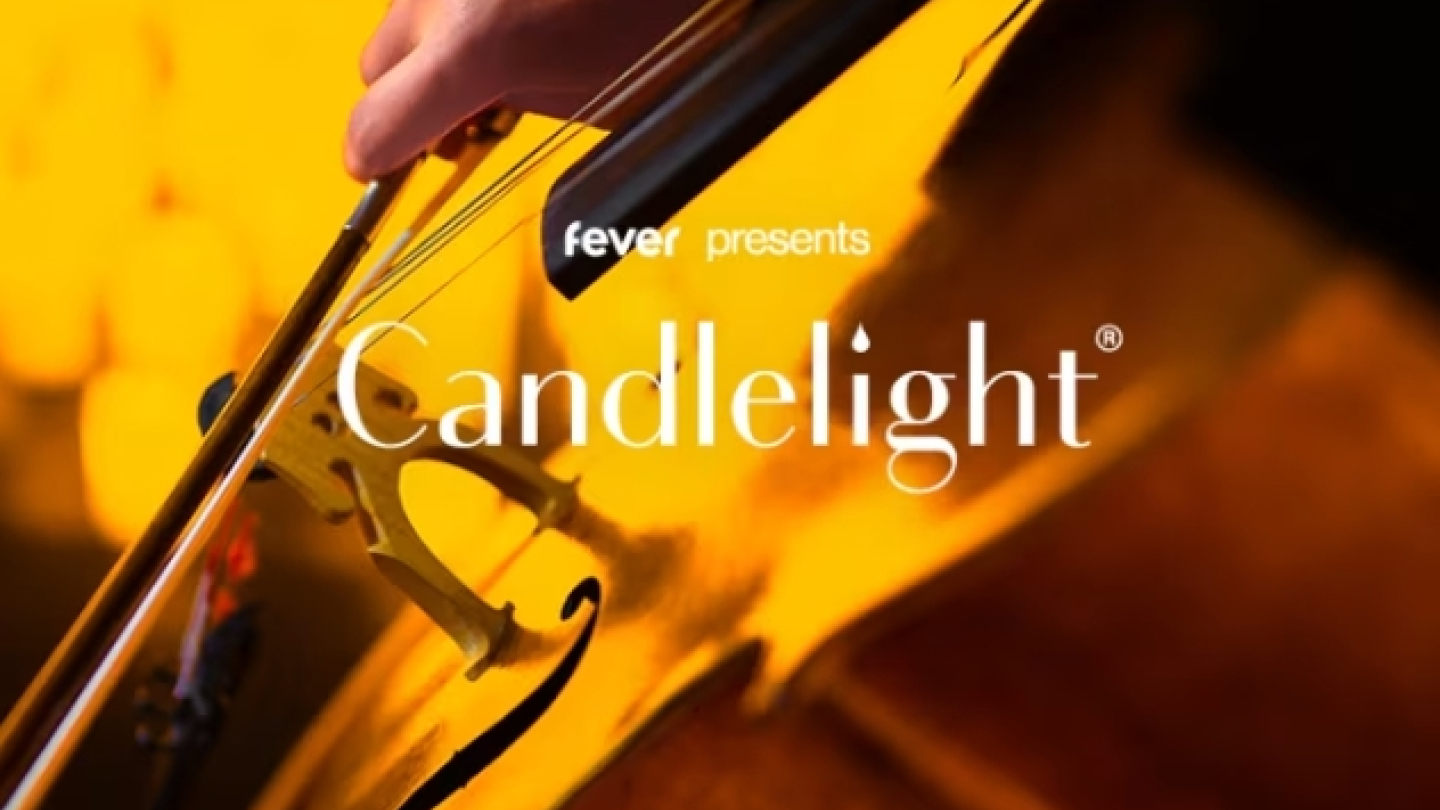Arte promocional da série de concertos Candlelight, da plataforma Fever, destacando um violoncelo em close durante uma apresentação. A cena é iluminada por uma luz dourada e quente, remetendo ao brilho das velas que caracteriza a experiência musical.