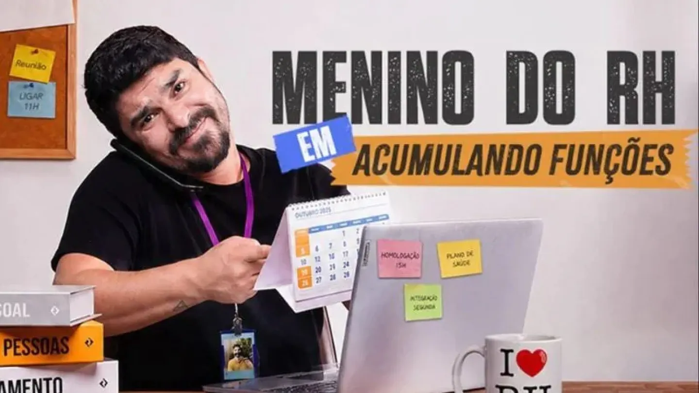 Cartaz promocional do espetáculo "Menino do RH em: Acumulando Funções". Em destaque, o humorista Michael Rodrigues aparece caracterizado como um funcionário de Recursos Humanos, sentado à mesa de escritório enquanto fala ao telefone e segura um calendário, transmitindo a ideia de multitarefa. Sobre a mesa há um notebook com lembretes coloridos, uma caneca escrita "I ❤️ RH", livros relacionados à gestão de pessoas e uma placa de identificação com seu nome. Ao fundo, um mural com recados reforça o ambiente co