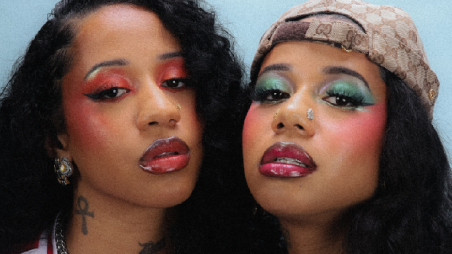 Foto promocional da dupla Tasha & Tracie em close, com as duas artistas lado a lado olhando para a câmera. Elas usam maquiagem marcante e colorida, cabelos longos e acessórios que reforçam sua identidade e estilo ligados ao universo do rap e da moda urbana.