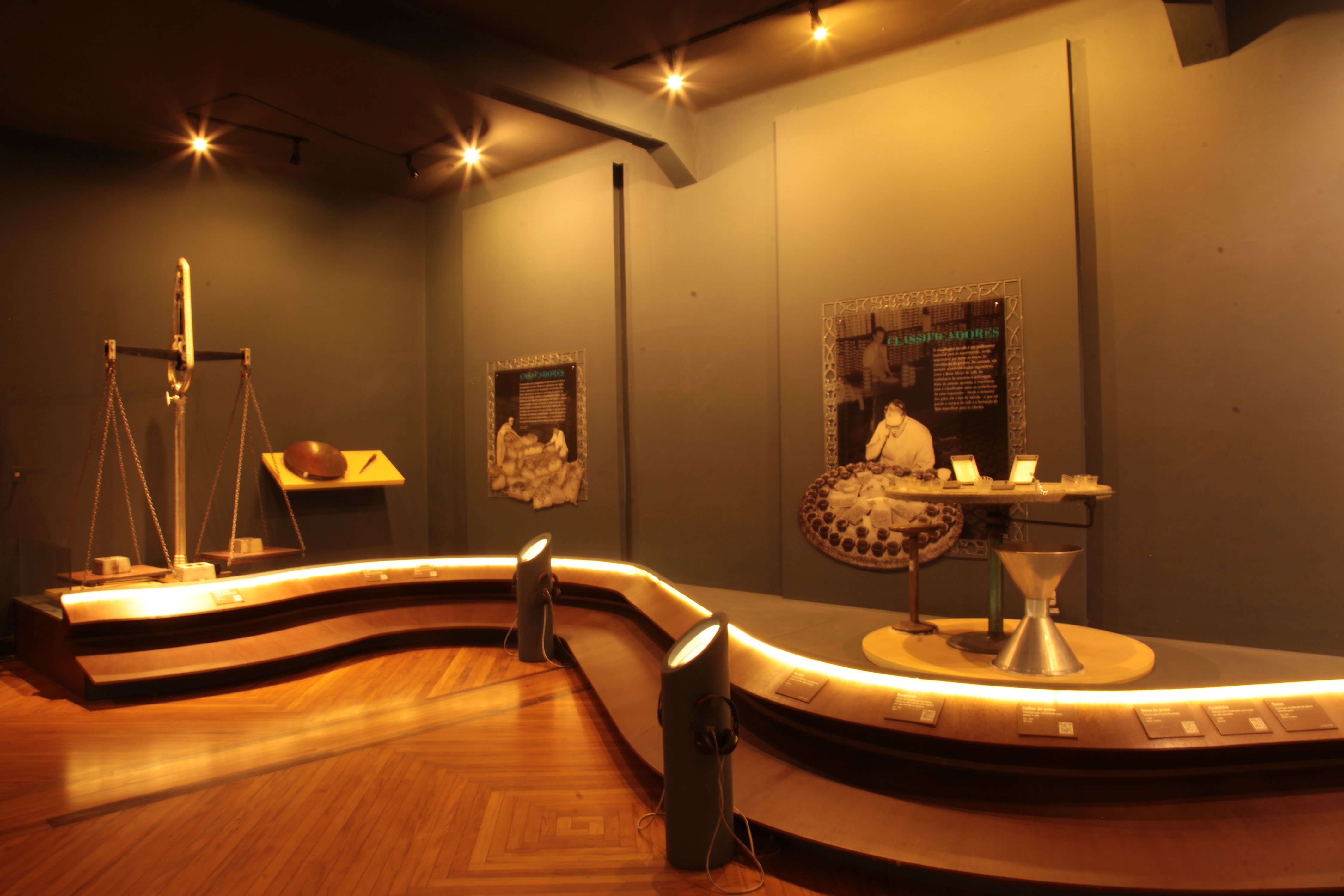 Sala de exposição com iluminação amarelada, exibindo objetos históricos e painéis informativos