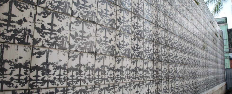 Um painel externo de azulejos antigos, com desenhos abstratos em preto e branco. Os azulejos estão desgastados pelo tempo e a imagem mostra o painel em perspectiva, diminuindo em direção ao lado direito