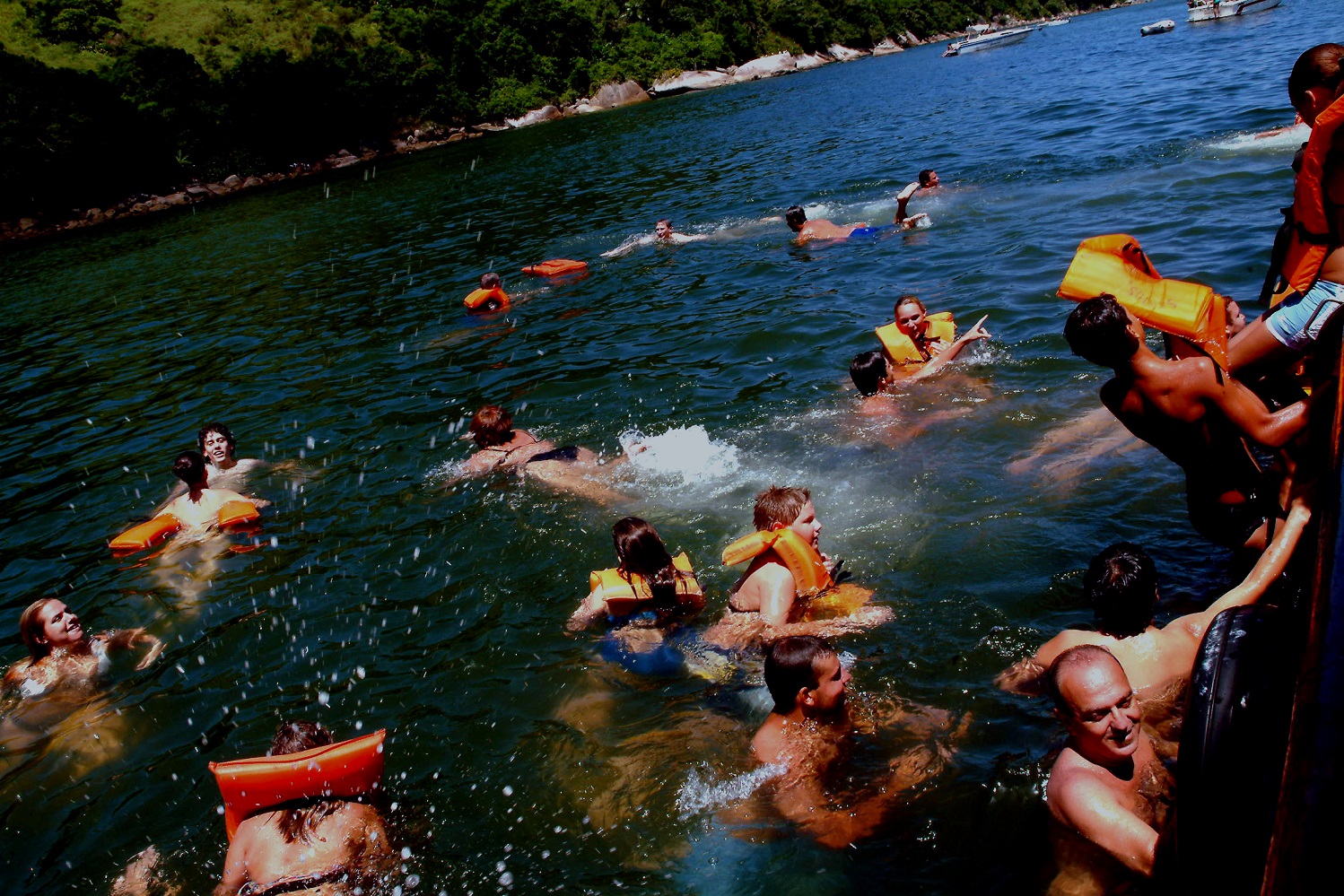 Pessoas nadando com colete salva vidas próximo à escuna