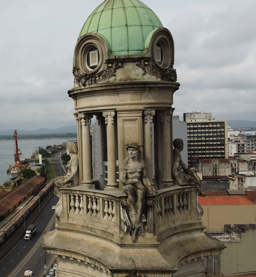 Cúpula verde da torre do edifício histórico da Bolsa do Café, com esculturas clássicas e vista para a orla portuária de Santos