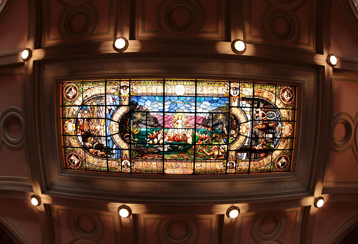 Vitral colorido no teto, com cenas artísticas e elementos decorativos detalhados