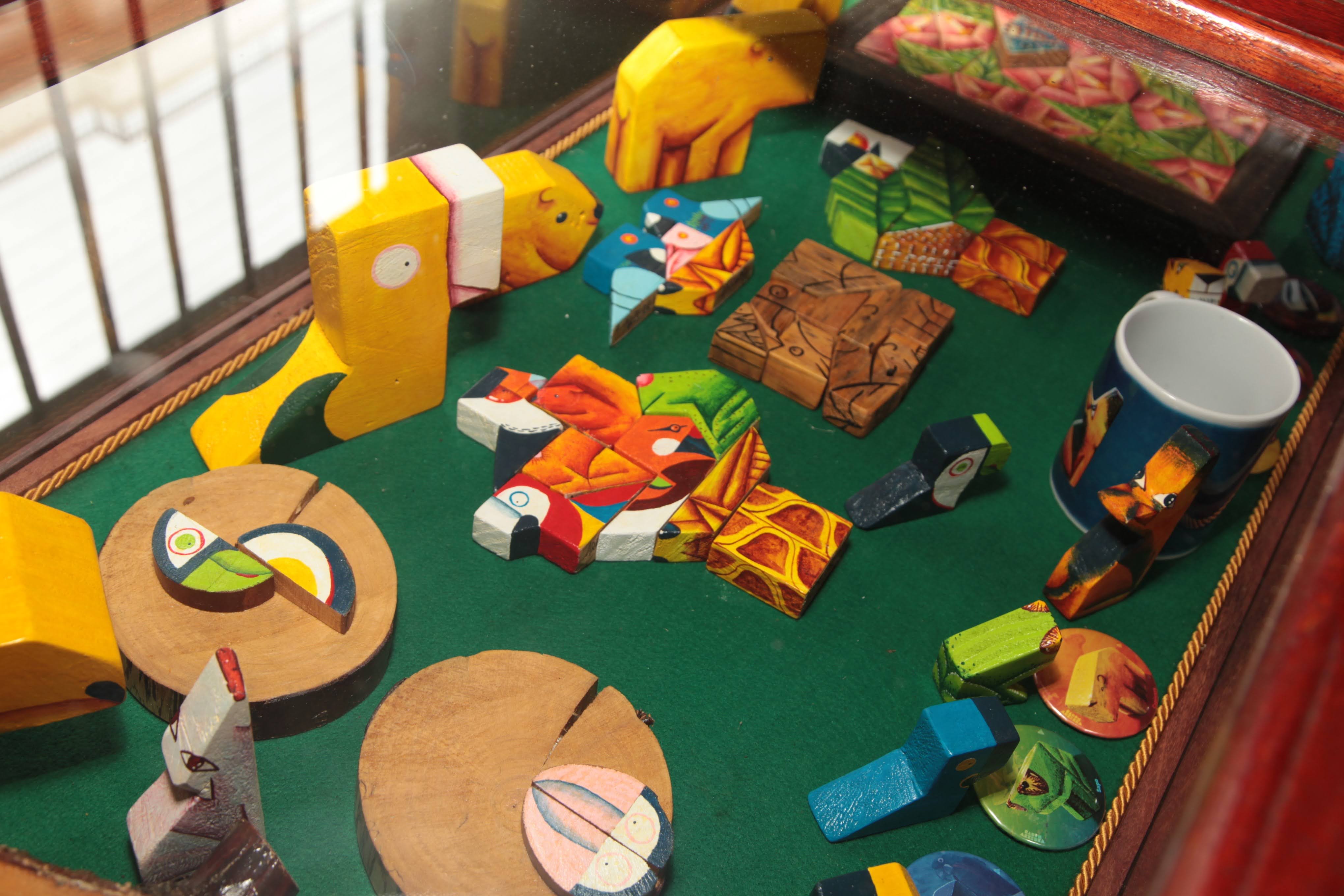 Vitrine com brinquedos de madeira pintados à mão e peças de encaixe coloridas, exibidas sobre feltro verde em estrutura de madeira com tampo de vidro