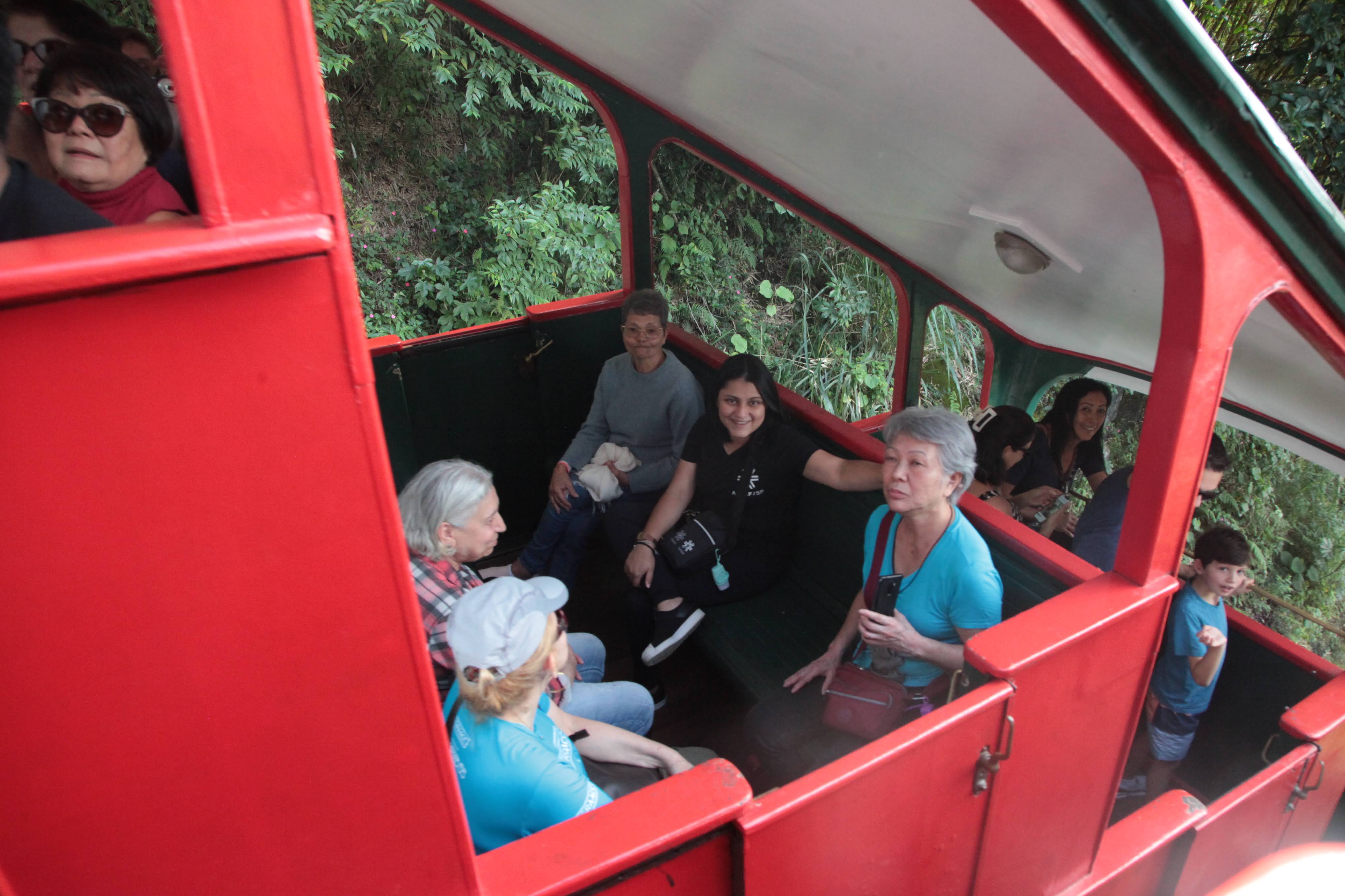 Vista desde el interior de un funicular rojo que muestra a varios pasajeros sentados y mirando alrededor mientras la cabina asciende o desciende en medio de la densa vegetación