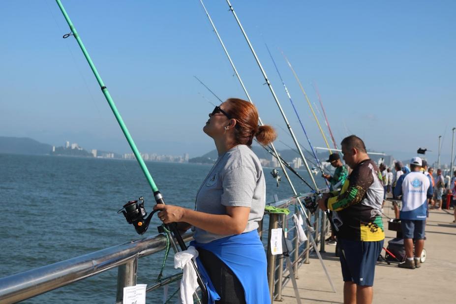 Personas pescando en el Deck del Pescador en Santos en un día soleado, con varias cañas de pescar alineadas junto al mar