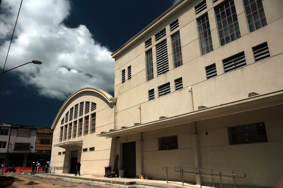 Uma vista de baixo e em ângulo de um edifício de arquitetura robusta, com fachada bege e janelas estreitas e alongadas, que combina uma seção com telhado em arco e outra retangular