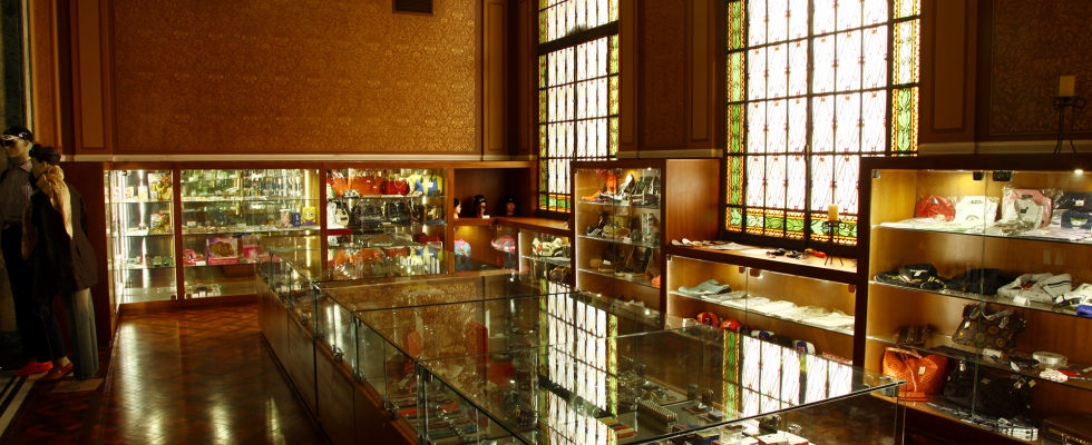 A imagem mostra o interior elegante de uma sala que parece ser uma exposição ou uma galeria/museu, possivelmente dedicada a objetos de luxo ou itens históricos relacionados à moda e acessórios.