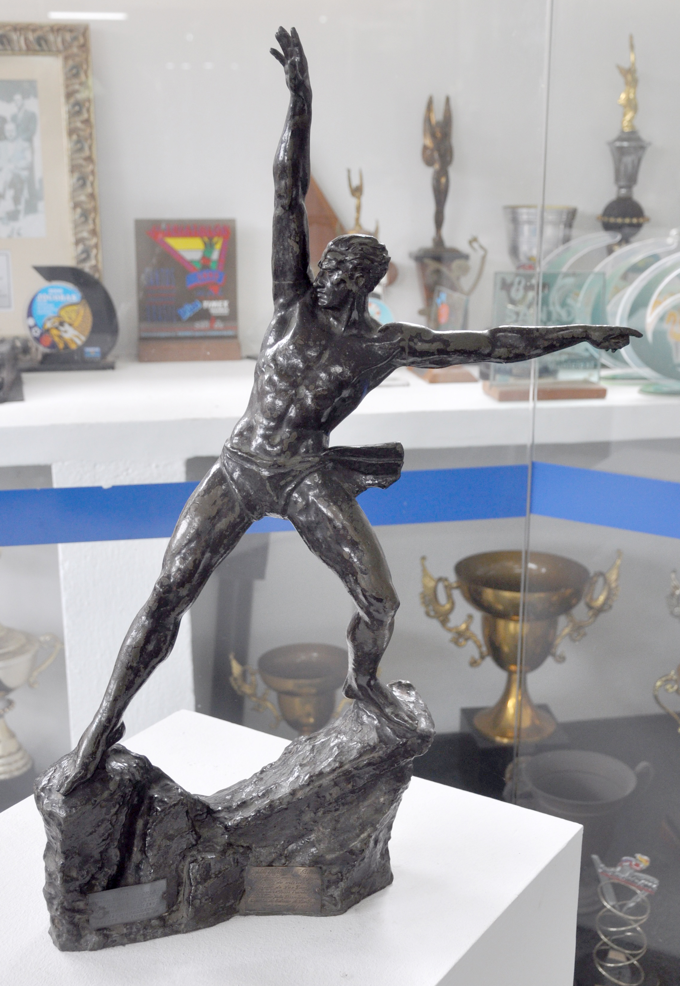 Uma escultura em bronze de um atleta em pose dinâmica destaca-se como um troféu em uma galeria esportiva