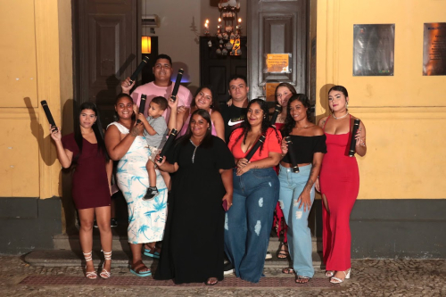 Um grupo de pessoas sorridentes posa com seus diplomas em frente à porta de um prédio antigo à noite