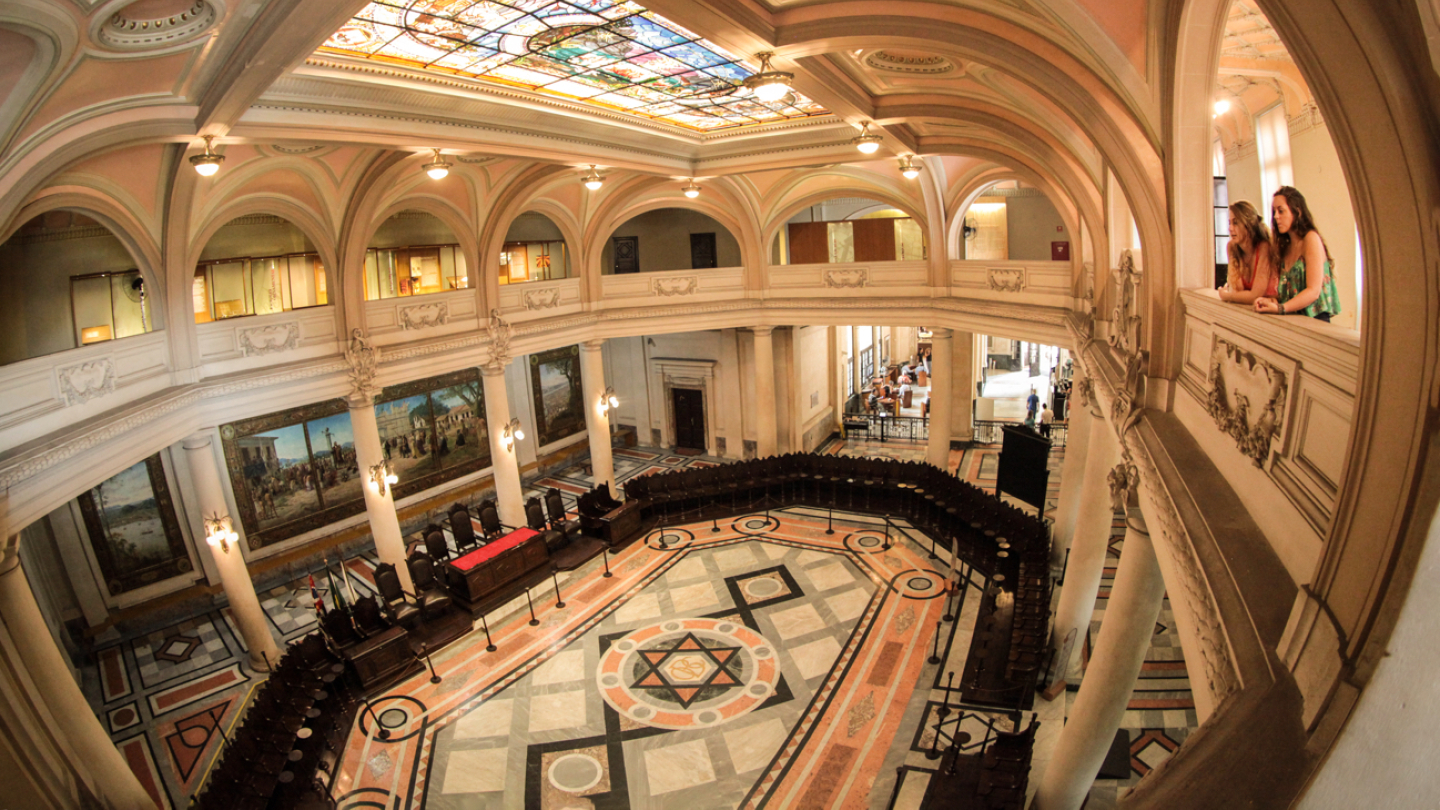 Salão nobre histórico com vitral colorido no teto, varandas internas e piso decorado