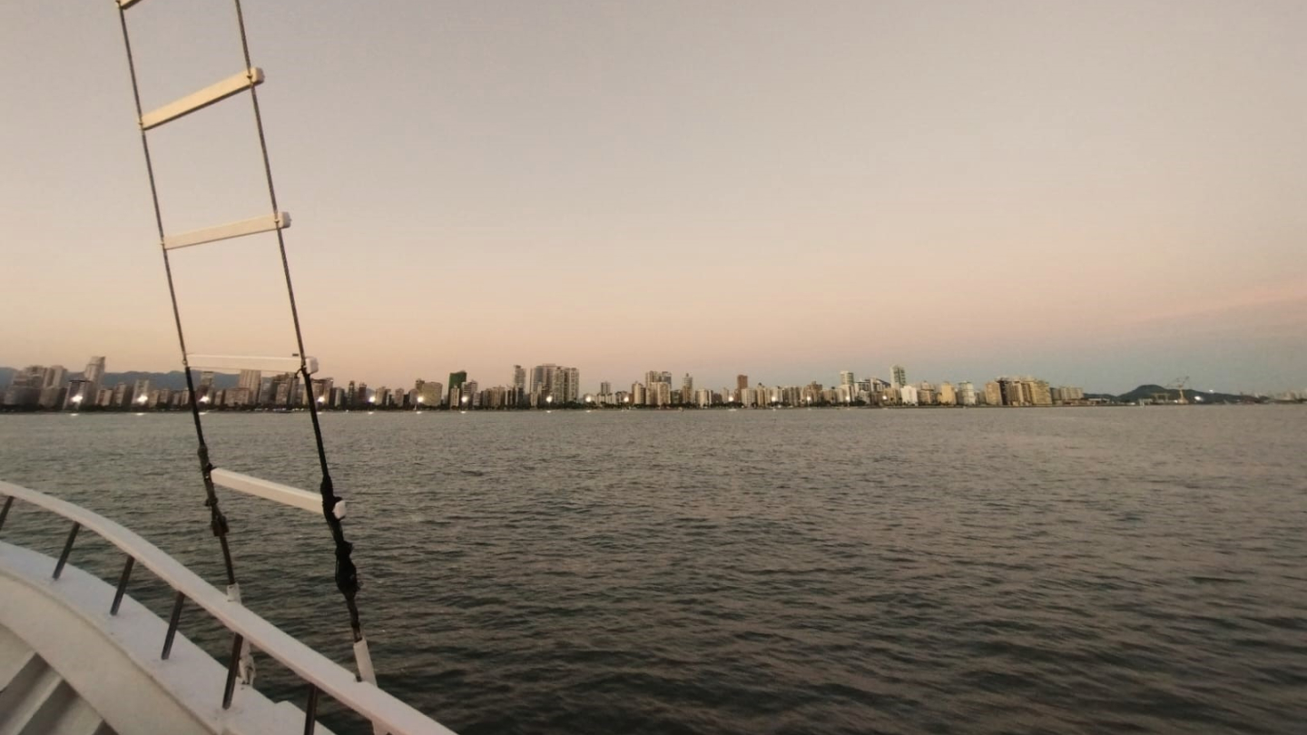 Vista dos prédios da orla de Santos, ao entardecer, e parte de uma escuna em primeiro plano