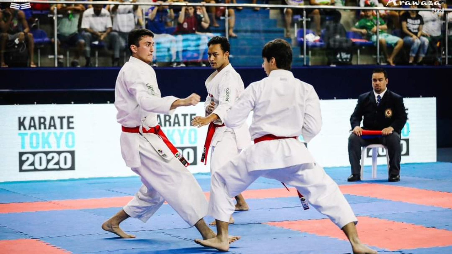 Demonstração de karatê, com 3 atletas de kimono e faixa vermelha