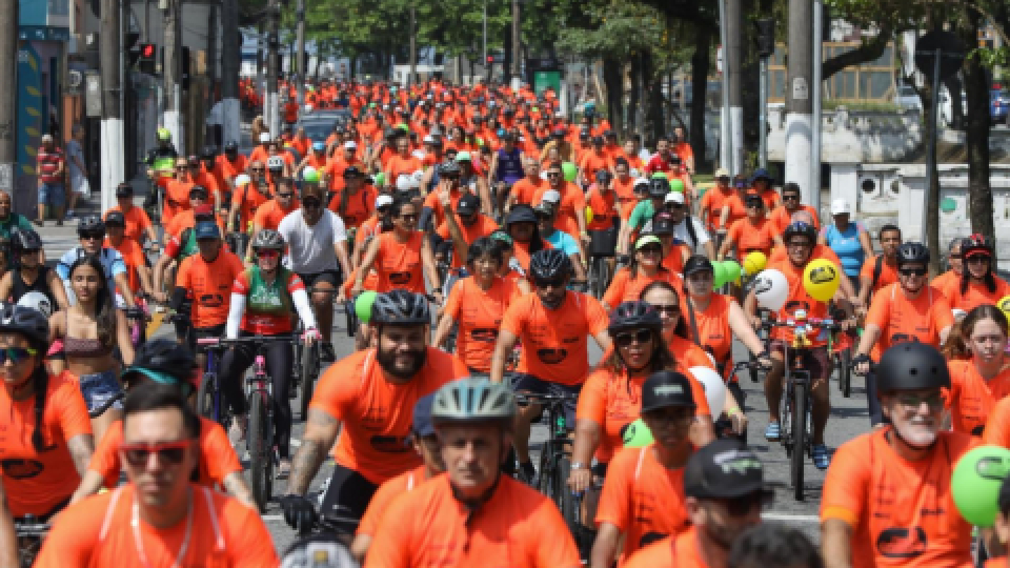 Multidão de ciclistas com camisetas laranjas participando de um evento nas ruas da cidade
