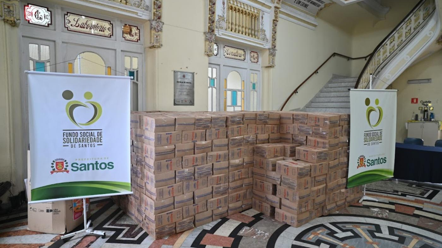 A imagem mostra a preparação de centenas de caixas de mantimentos que serão destinadas a famílias em situação de vulnerabilidade social em Santos. A iniciativa é do Fundo Social de Solidariedade de Santos, em parceria com a Prefeitura Municipal, reforçando o compromisso de cuidar de quem mais precisa.