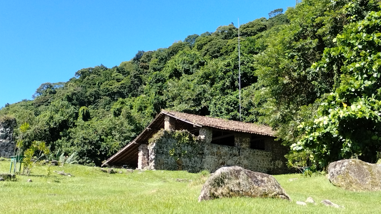Engenho de pedra antiga em meio à natureza, cercada por árvores e gramado com grandes rochas