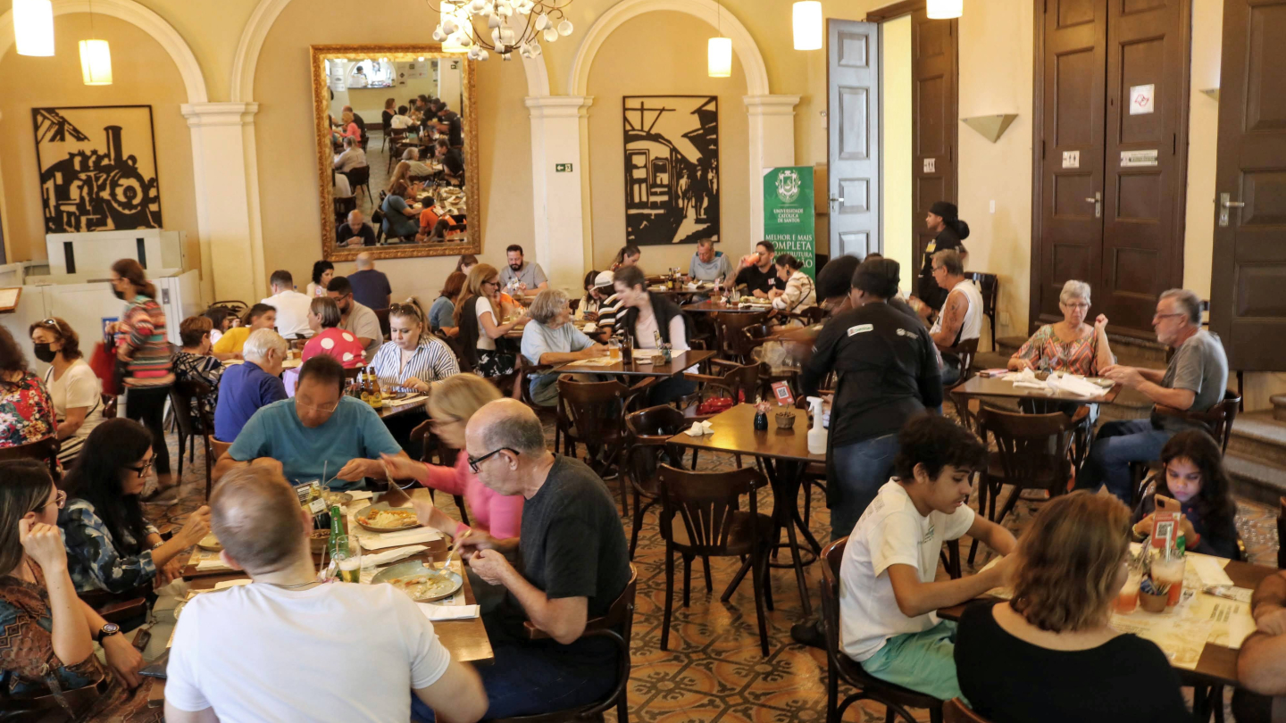 Restaurante movimentado, com várias mesas ocupadas por pessoas almoçando em ambiente acolhedor e decorado