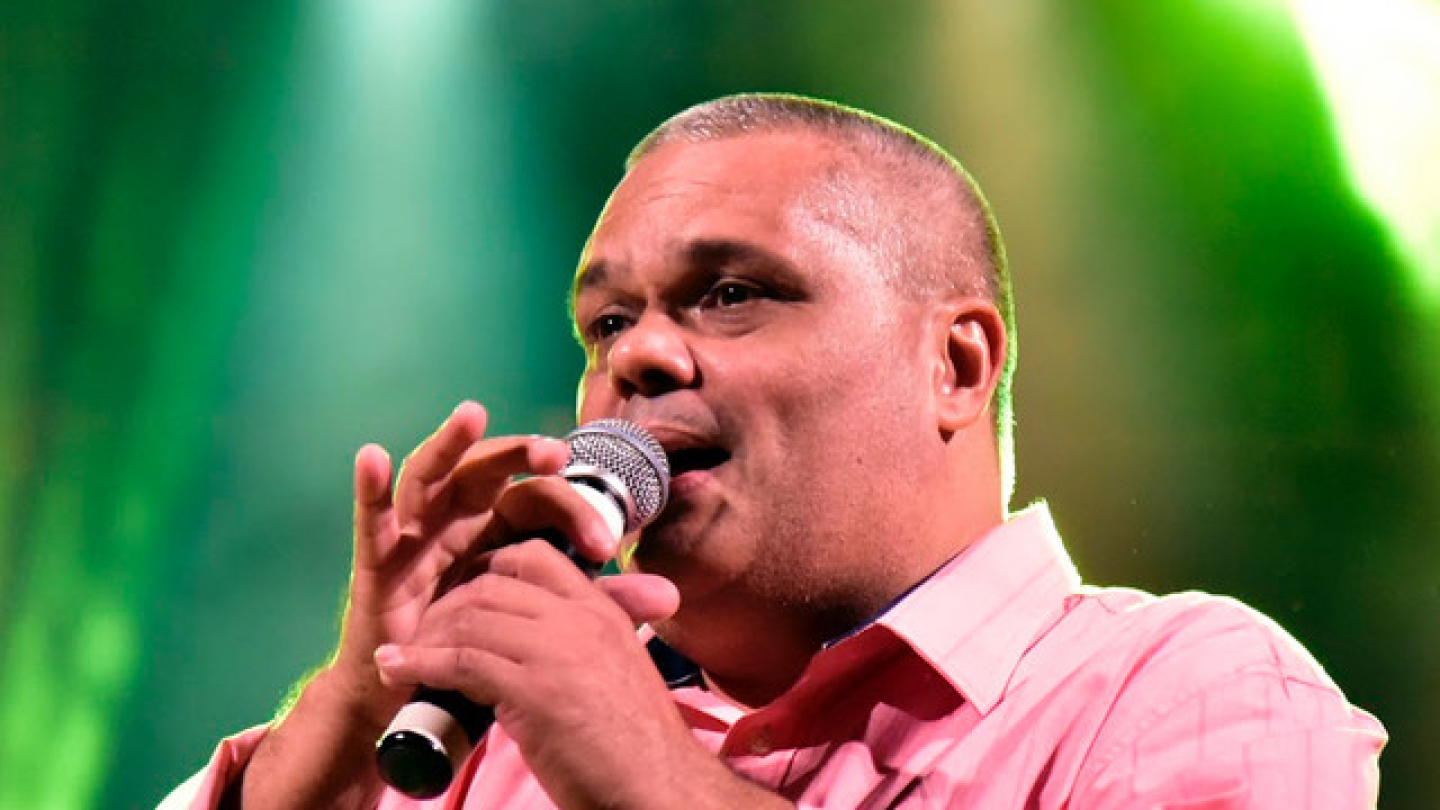 Homem com microfone e camisa rosa