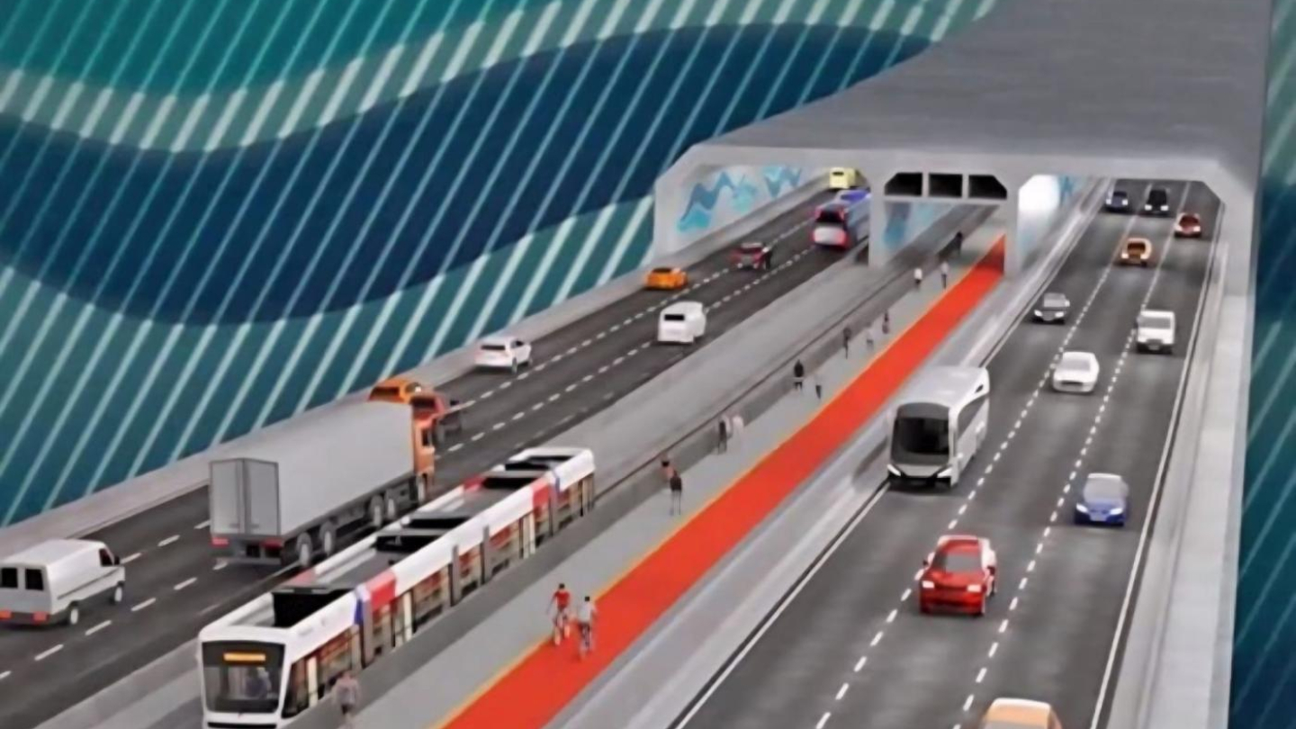 A imagem mostra uma arte conceitual do futuro túnel Santos-Guarujá. O projeto apresenta uma estrutura moderna, com várias faixas de tráfego para automóveis, caminhões e ônibus, além de um corredor exclusivo para o VLT (Veículo Leve sobre Trilhos). Ao lado, há uma faixa destinada a pedestres e ciclistas, destacada em vermelho.