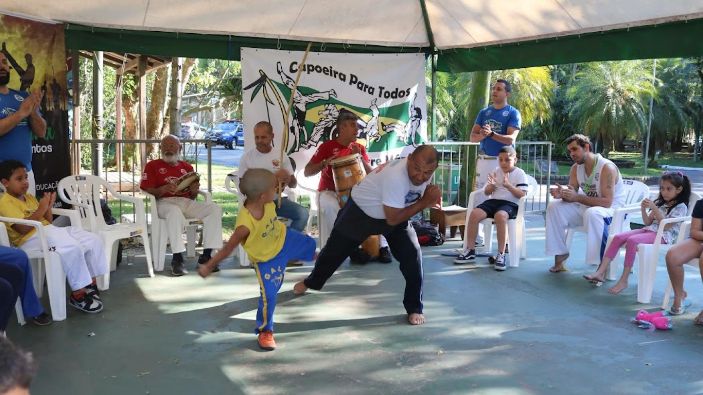 Roda de capoeira, com atletas lutando e músicos ao redor com berimbau