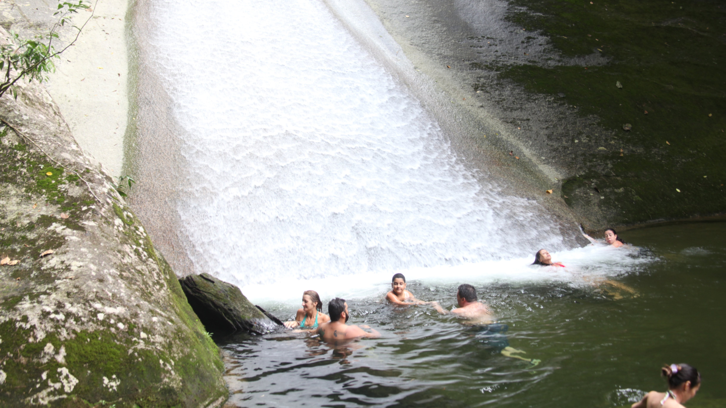 Pessoas se divertem em cachoeira com tobogã natural formado por pedras e água corrente