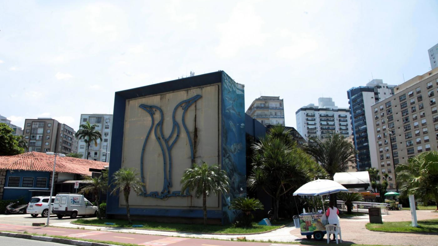 Fachada lateral do Aquário Municipal em Santos, com silhueta de 2 pinguins em azul