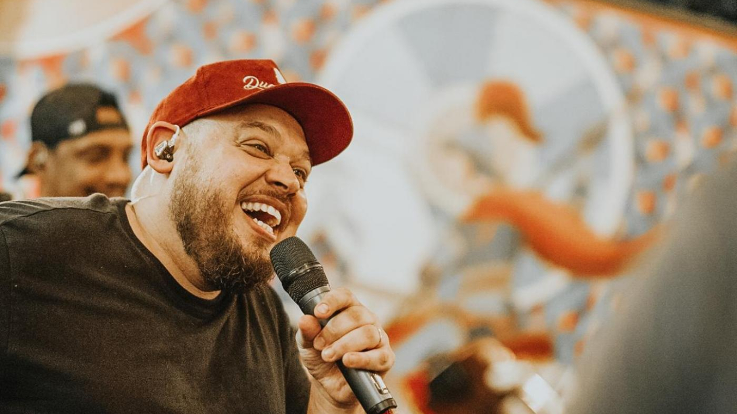 Cantor Ederson Santos, com microfone em mãos, num cenário de cores claras