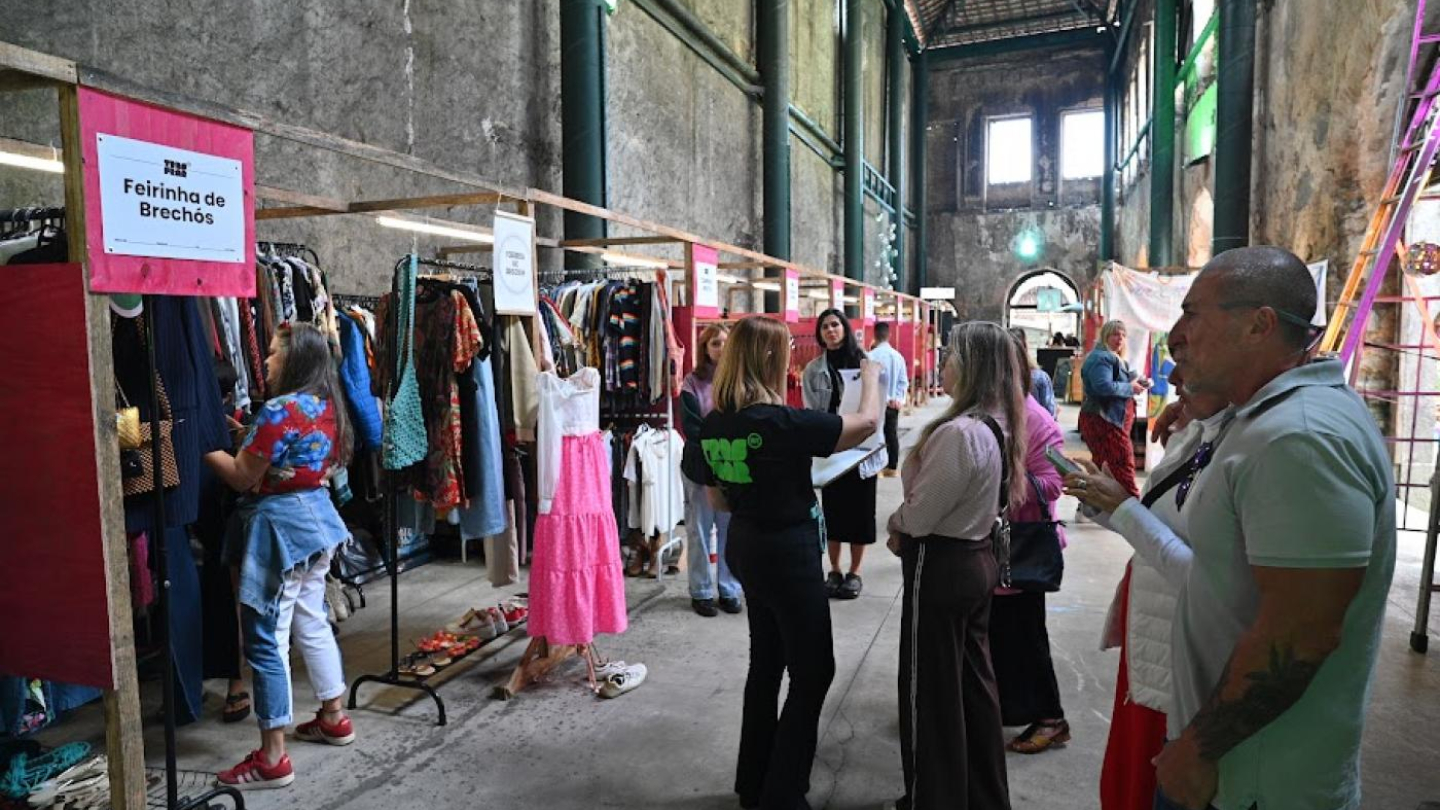 Feira de artesanato na Frontaria Azulejada, expositores de roupas e pessoas circulando pelos estandes