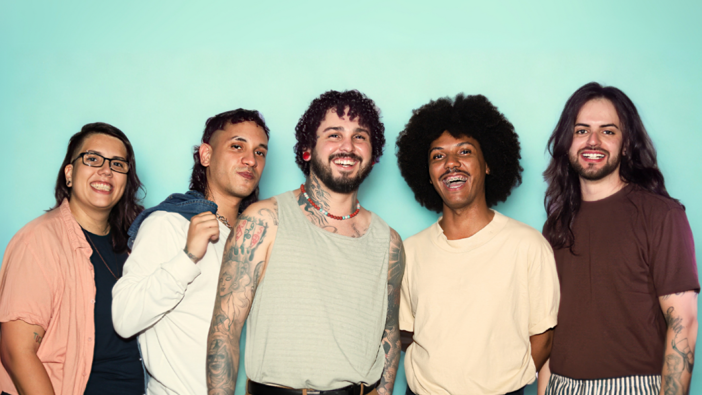 Grupo de cinco pessoas posa sorridente diante de um fundo azul-claro