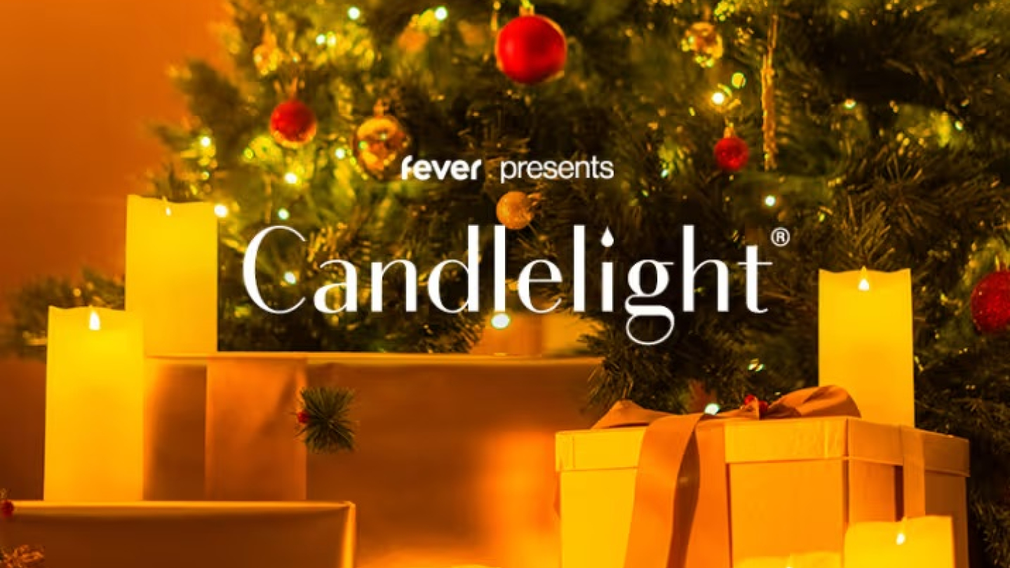 Uma imagem com iluminação quente, em tons de laranja e dourado, foca em presentes embrulhados e velas acesas dispostas na base de uma árvore de Natal decorada, com o logo da Fever e o nome "Candlelight" ao centro