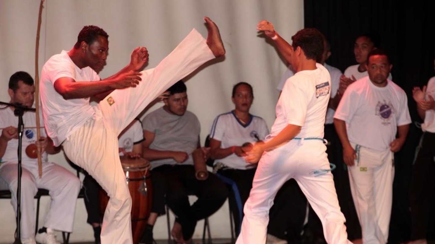 Roda de capoeira, com atletas lutando e músicos ao redor com berimbau