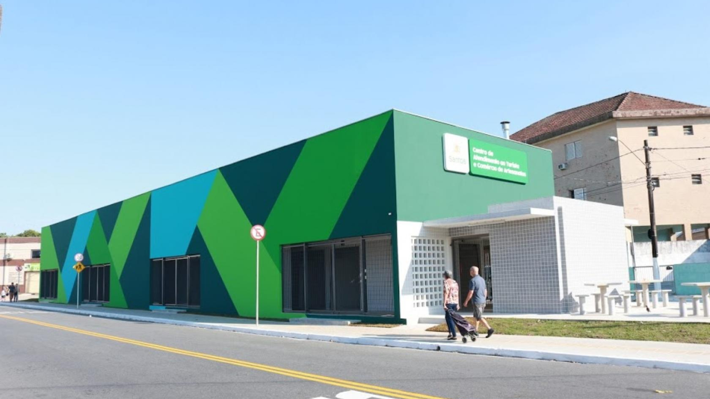 Um edifício moderno de um andar, com fachada decorada em tons geométricos de verde e azul, exibe uma placa indicando ser um "Centro de Atividades", em um dia ensolarado