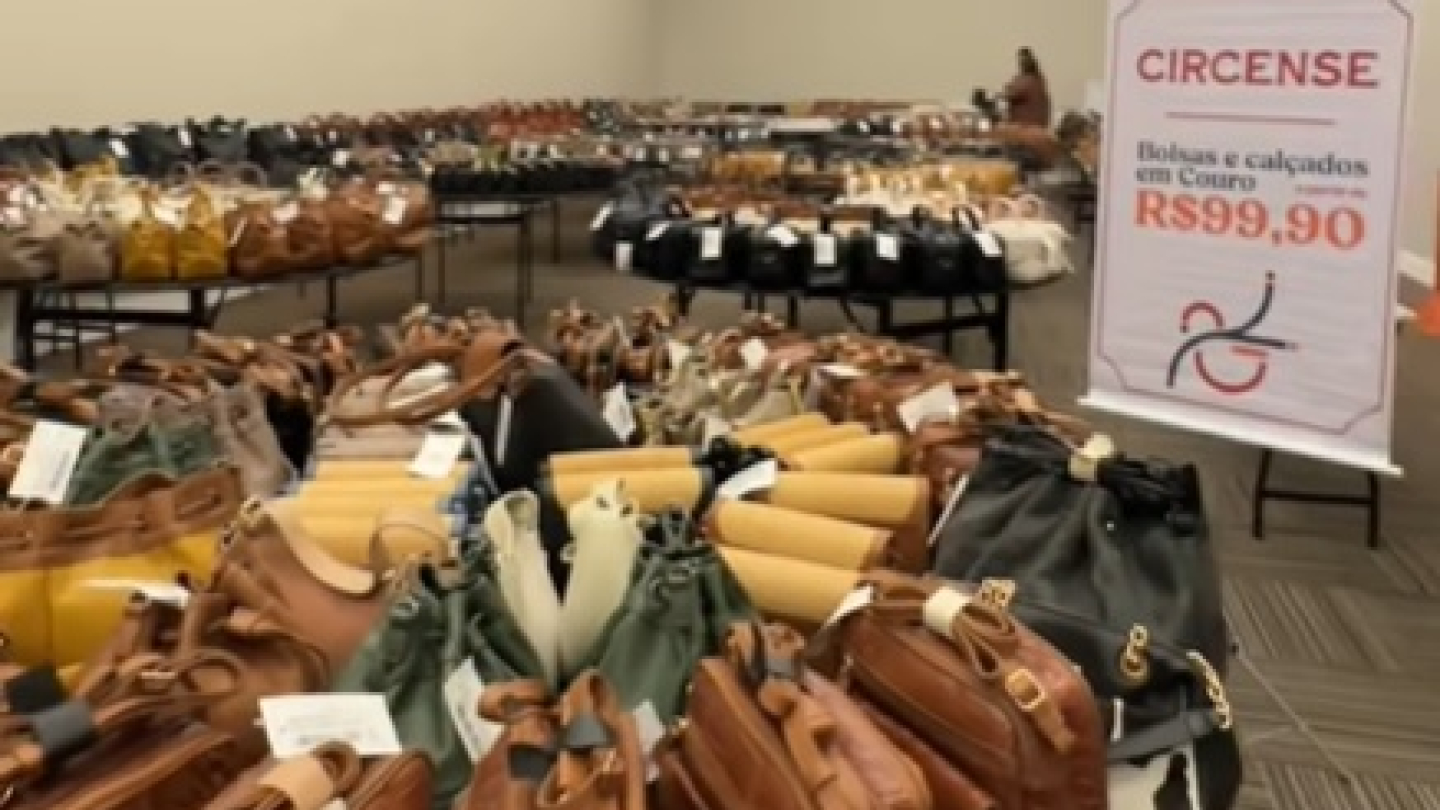 Várias prateleiras de bolsas e calçados de couro, com cartaz a partir de R$99,90