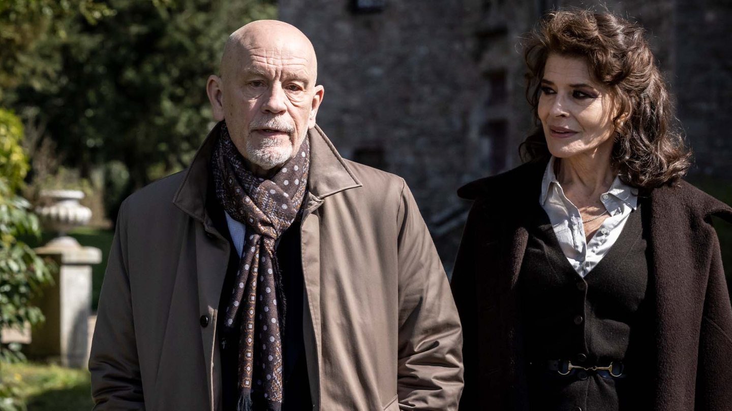 A imagem mostra dois atores, John Malkovich e Fanny Ardant, em um ambiente externo, em cena do filme "Sr. Blake ao Seu Dispor"