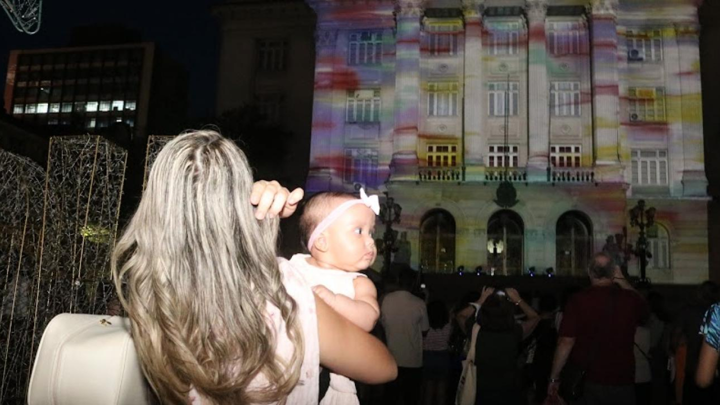 Mãe e bebê em frente ao Palácio da Prefeitura iluminado