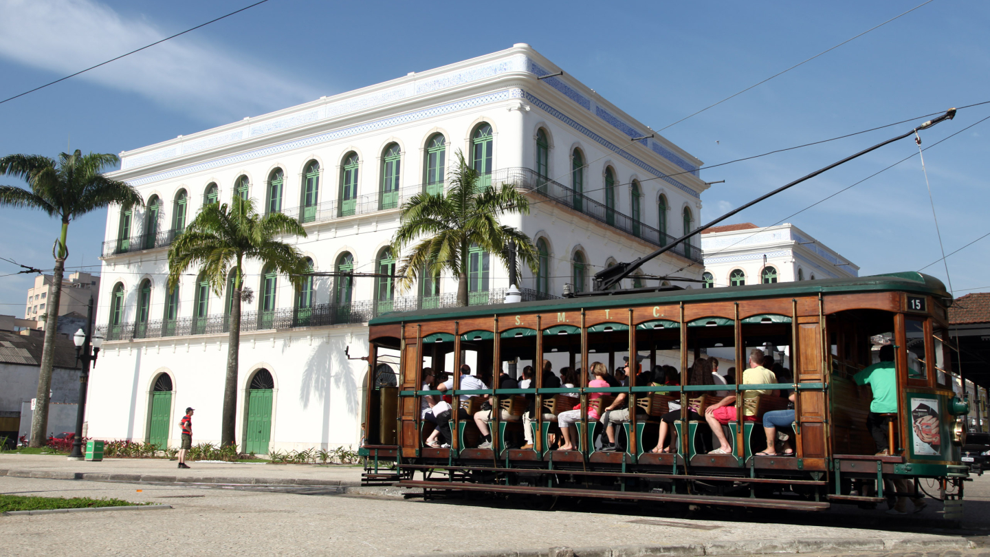 Bonde cheio de pessoas com museu pelé ao fundo.