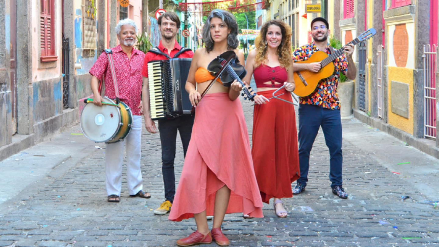 Uma imagem vibrante de um quinteto musical posicionado em uma rua estreita de paralelepípedos, ladeada por prédios coloridos e rústicos