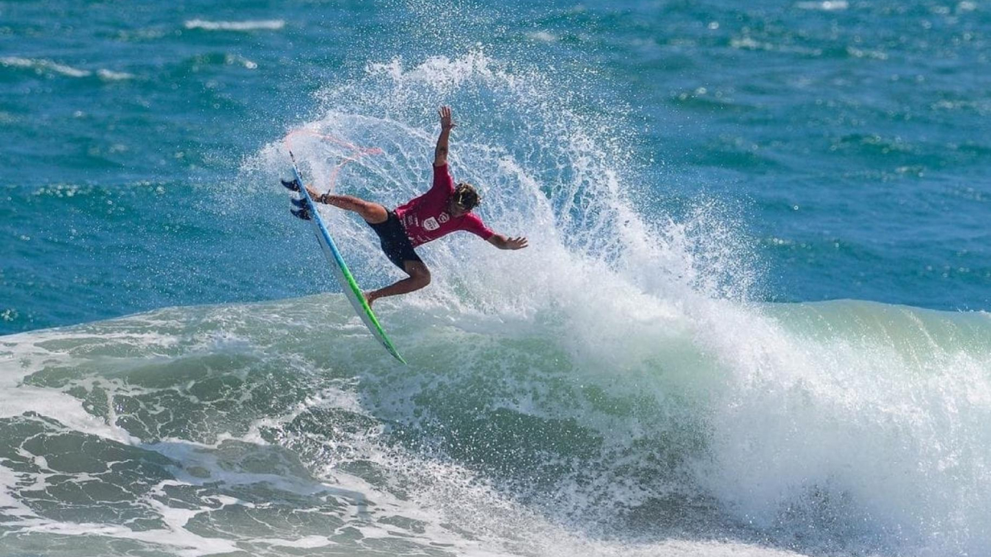 Surfista executa uma manobra aérea radical sobre a onda, levantando um grande spray de água no mar