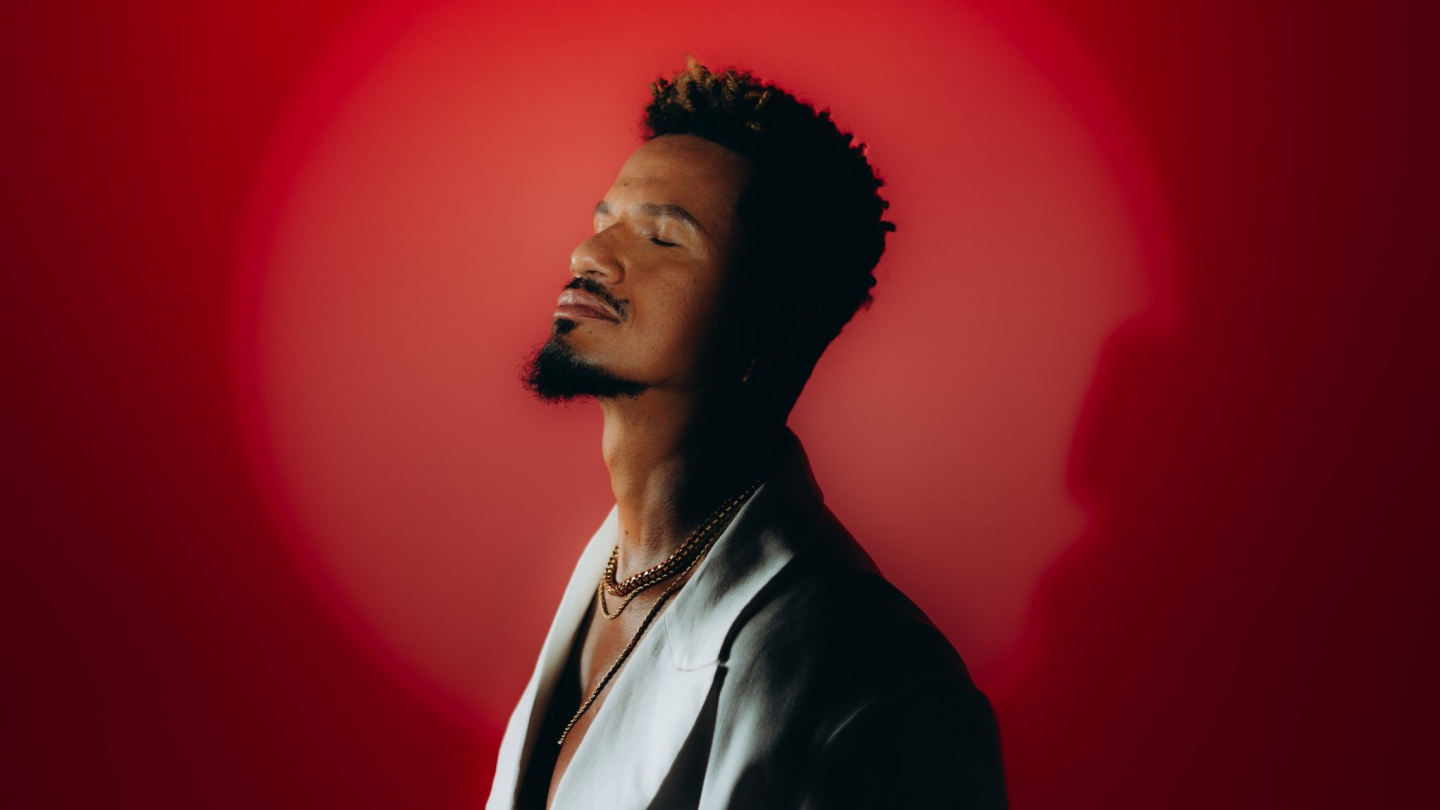 A fotografia apresenta um close-focado no cantor e compositor Zé Manoel de perfil, com os olhos fechados e expressão serena, posando contra um fundo vermelho iluminado de forma circular